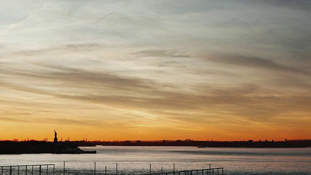 日落时纽约港上空戏剧性的天空，远处自由女神像的剪影/美国纽约州纽约市视频下载