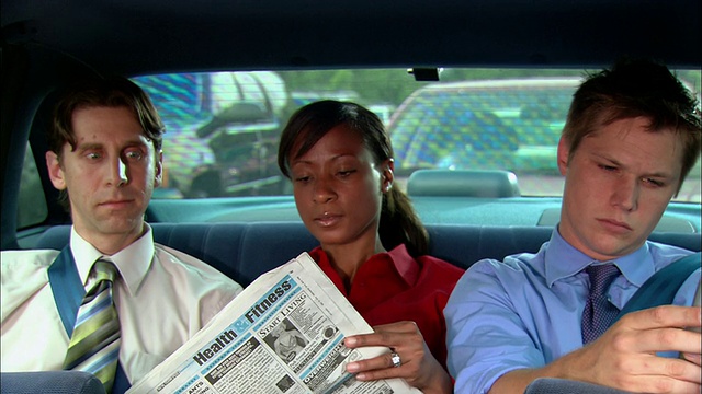 在汽车后座上，一个中等镜头的女人正不舒服地坐在两个男人中间/看报纸视频下载