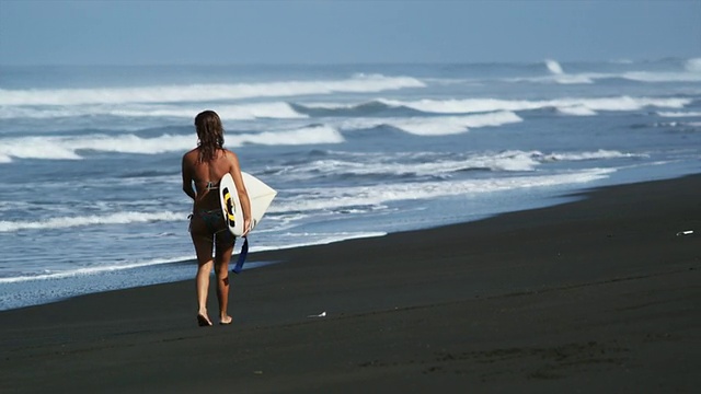 一个女人带着冲浪板在海滩上散步视频下载