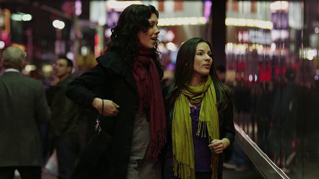 美国纽约州纽约，两个年轻的女人在晚上看时代广场的橱窗视频下载