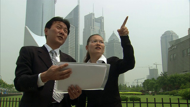 中景一对商人在摩天大楼的背景下看着文件，指着天空/上海视频下载