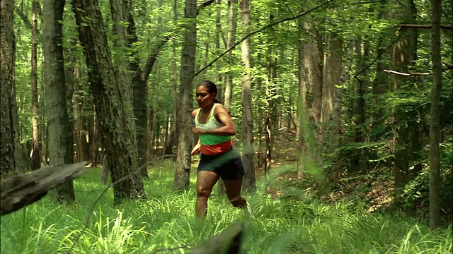 一名女子跑出树林小径/踩过原木经过摄像机/红顶山州立公园，乔治亚州视频素材