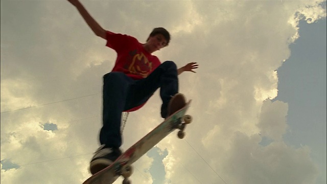 低角度拍摄的杆子对天空的云/慢动作的溜冰者表演奥利在镜头上视频下载
