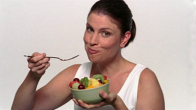 中镜头的女子一边吃着水果沙拉，一边看着镜头视频素材