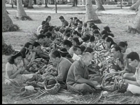 1949年B/W蒙太奇户外宴会。马绍尔群岛的Likiep，一大群成年人和儿童坐在地上两排，用手吃饭视频下载