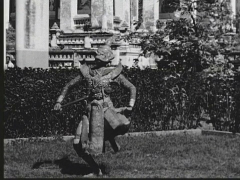 1948 B/W蒙太奇巨大的恶魔神像矗立在庙宇前。泰国，Bango，两名男子穿着精心制作的服装，在仪式舞蹈中重演战斗妖神和钱神的传说视频下载