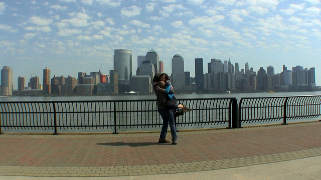 美国新泽西州泽西城，一对年轻的夫妇在码头上奔跑拥抱，背景是纽约市的天际线视频素材