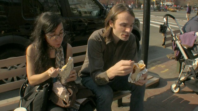 一对年轻夫妇在美国新泽西州纽约市中心/泽西城的长椅上吃沙拉三明治视频下载
