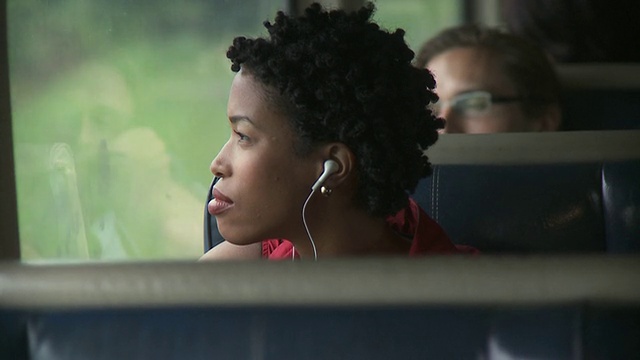 一名女子坐在行进中的火车靠窗处，用便携式媒体播放器听音乐，用手机聊天/美国纽约市视频下载