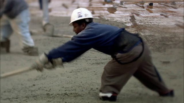 建筑工人站在湿漉漉的水泥地上，用铁锹把它铲平/在水泥地上倾斜腿/纽约市视频下载