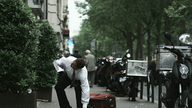 一个商人拖着一个手提箱走在欧洲城市的街道上，一边看地图视频下载