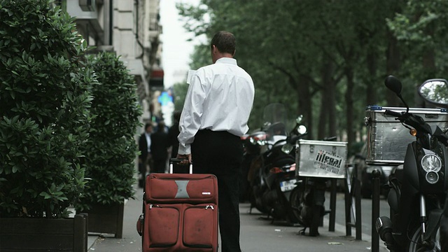 一个商人拖着一个手提箱走在欧洲城市的街道上，一边看地图视频素材