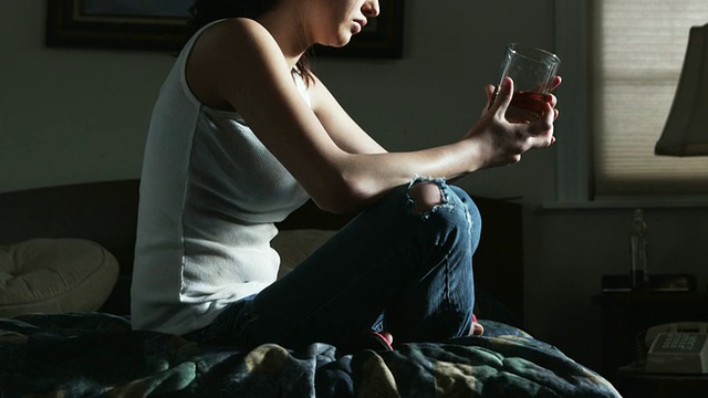 受虐妇女坐在床上，手里拿着一杯酒视频素材