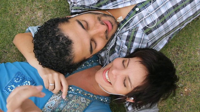 在古巴哈瓦那，一对夫妻躺在草地上分享手机和音乐视频下载