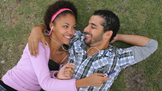 古巴哈瓦那，一对年轻夫妇躺在草地上听音乐，共用耳机视频下载