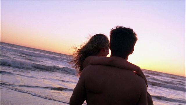 慢动作中镜头，一名男子抱着一名女子进入日落/太平洋的海浪中视频下载