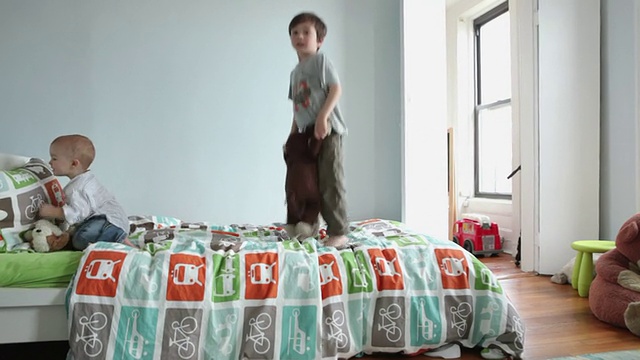 两个男孩(17个月，4-5岁)在卧室的床上跳，纽约，美国视频素材
