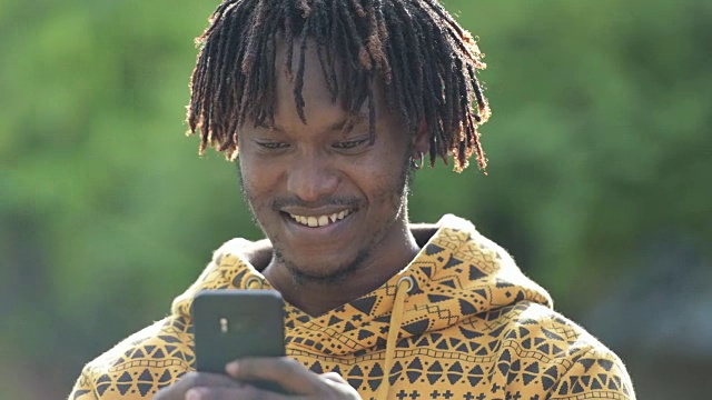 年轻快乐英俊的非洲男子微笑，同时使用电话在街道户外视频素材