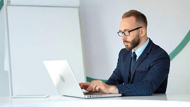 漂亮的商人穿着西装，戴着眼镜，在白色的办公室里用笔记本电脑工作视频素材