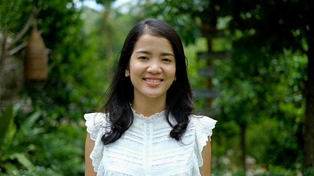 快乐年轻的亚洲妇女在白色西装微笑和笑对绿色的自然背景视频素材
