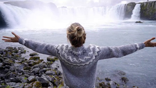年轻女子张开双臂，前方是冰岛壮丽的戈达佛斯瀑布。人旅游探险概念4K视频素材