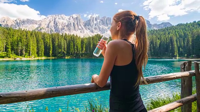 一名女子在山湖休息，用可重复使用的水瓶补水视频下载