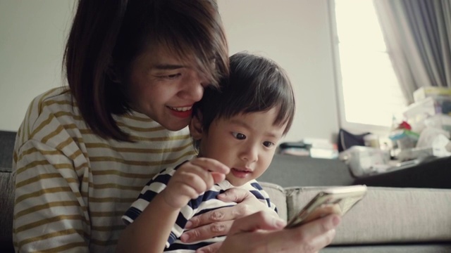 年轻的妈妈和快乐的宝宝(12-23个月)在家里使用智能手机视频素材