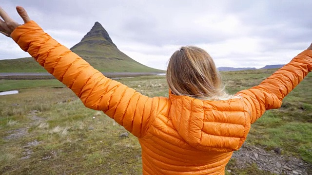 冰岛的年轻女子在著名的Kirkjufell山的春天阴云密布的天空中张开双臂争取自由视频素材