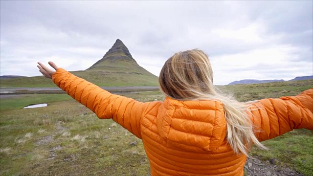 冰岛的年轻女子在著名的Kirkjufell山的春天阴云密布的天空中张开双臂争取自由视频素材