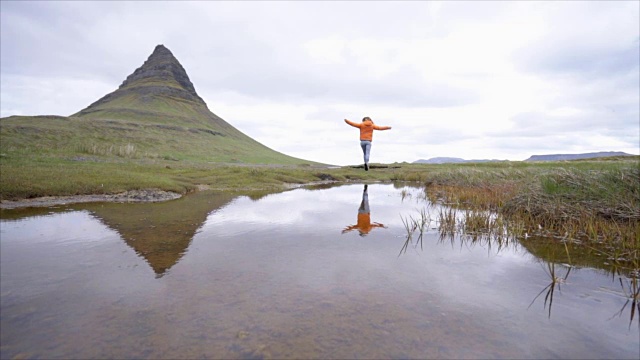 冰岛的年轻女子在著名的Kirkjufell山的春天阴云密布的天空中伸出双臂争取自由视频素材