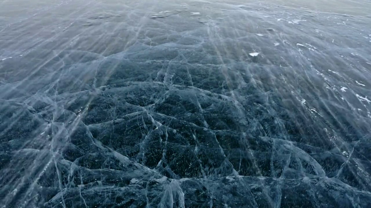 雪在冰面上飞舞。雪花在贝加尔湖的冰面上飞舞。冰非常美丽，有独特的裂缝。雪花闪耀着红光。在日落时分。高对比度。视频下载