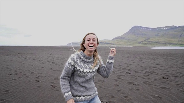 年轻女子的手臂伸展在大海上站在黑色的沙滩上，头发在风中-冰岛-女性跑步嬉戏享受自然和自由-慢动作视频素材