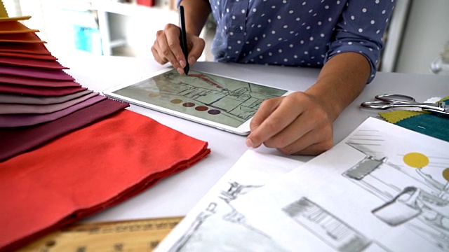 一个面目全的室内设计师在平板电脑上工作，用桌子上的织物样品尝试设计的颜色视频素材