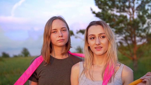 两名年轻女子体操运动员的肖像与体操器材在山上在夏季日落视频素材