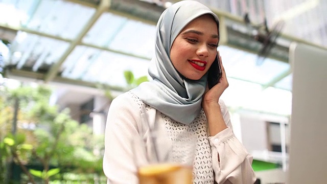 美丽的马来西亚女人戴着头巾，在咖啡馆里打电话视频下载