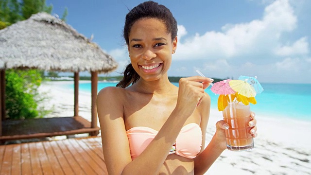 年轻的少数民族女性在海滩上享受多彩的鸡尾酒视频素材