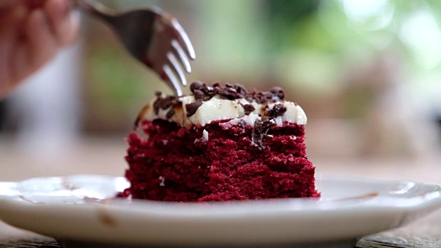 一个女人用叉子切一块红色天鹅绒蛋糕奶油和巧克力在白色陶瓷盘子在木桌上视频素材