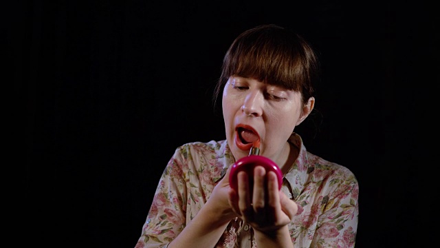 一名年轻女子在黑色的背景下涂上红色的口红。视频素材