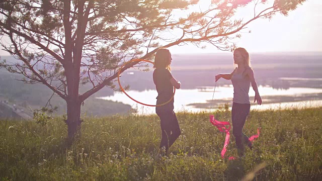 在日落时分，柔韧的妇女在山上用体操带和铁环练习视频素材