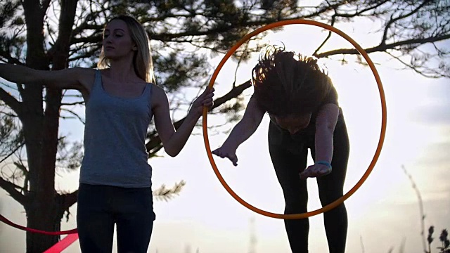 日落时分，两名年轻女子在树下用体操胶带跳圈视频素材