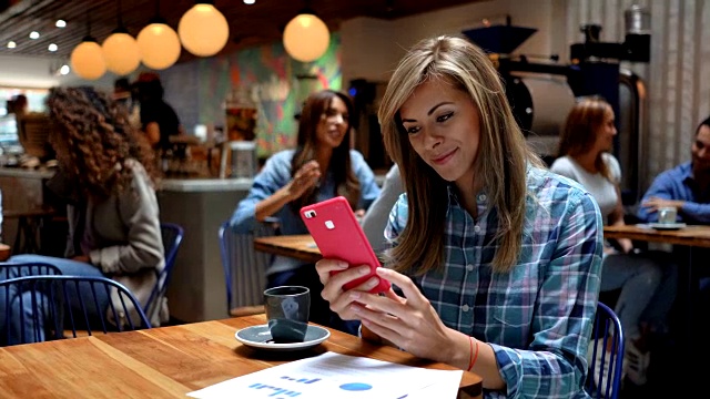 美丽的女人在咖啡馆享受咖啡和聊天在她的智能手机微笑视频素材