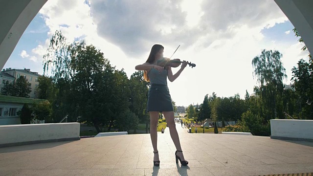有魅力的女人站在公园前的拱门下拉小提琴视频素材