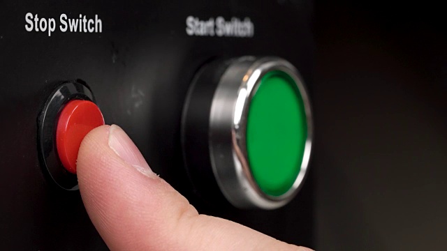 帧中的两个按钮的特写。绿色启动开关和红色停止开关按钮。手指按下红色停止开关按钮。视频下载