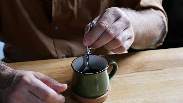 在厨房里，一个留着胡子的老头把勺子转进一杯咖啡里视频下载