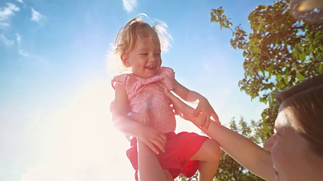 SLO MO微笑的小女孩被她的妈妈带到天空的阳光下视频素材