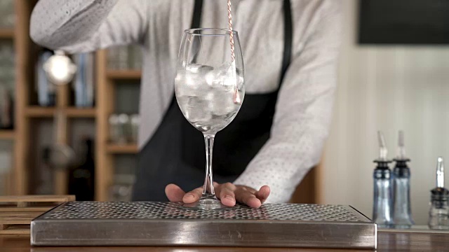 特写的一个调酒师把冰块放入玻璃杯，然后把冰块在玻璃杯中使用酒吧勺子。视频素材