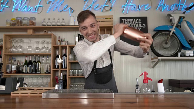 一位英俊的年轻酒保站在吧台前用鸡尾酒调酒器摇着鸡尾酒。天赋调酒。视频素材