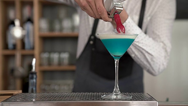 特写英俊的年轻酒保的手添加一个发泡奶油到蓝色的鸡尾酒。在吧台完成了一杯蓝云鸡尾酒。视频下载