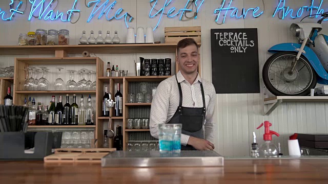 一个英俊的年轻的调酒师倒一个蓝色的库拉索酒与冰块在吧台。视频素材