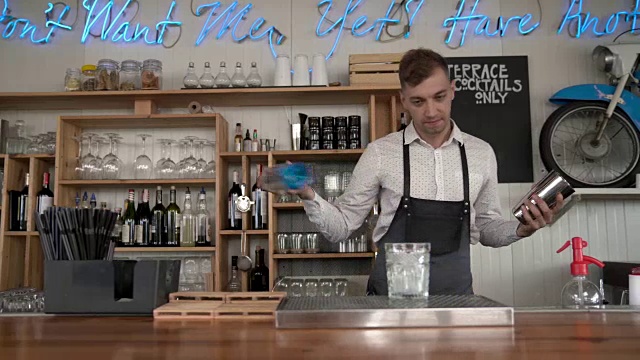 天赋调酒。一个英俊的年轻的调酒师把蓝色的库拉索酒倒入一个有冰块的杯子。视频素材